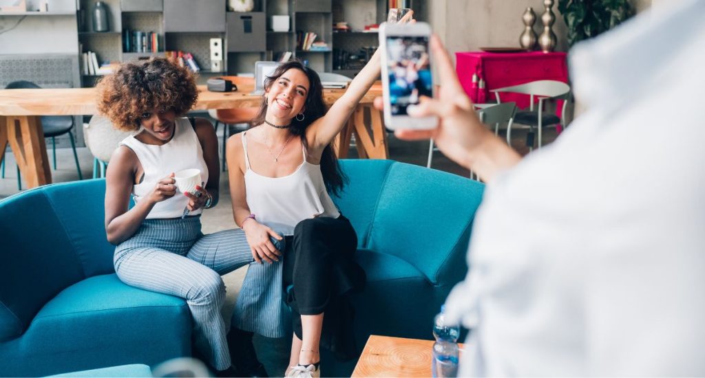 Friends enjoying coffee and taking a casual photo together on a smartphone — authentic social media lifestyle moment.