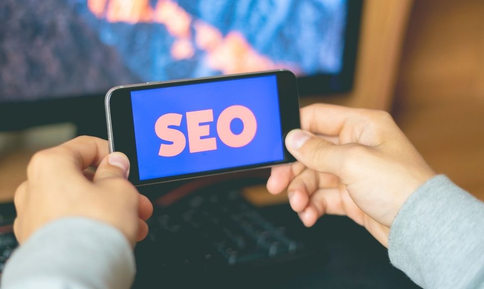 Person holding a smartphone displaying the word “SEO” in bold letters, symbolising search engine optimisation and Answer Engine optimisation for digital marketing success.