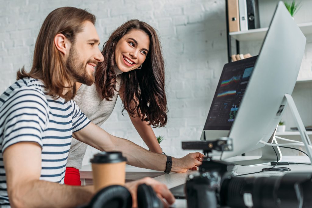 Two creative professionals collaborating on a computer project in a modern office, reviewing marketing visuals on a large desktop screen — concept of teamwork and digital personalisation.