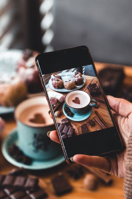 A person taking a photo of coffee and desserts for social media, illustrating the role of creative content in paid strategies and hybrid marketing.