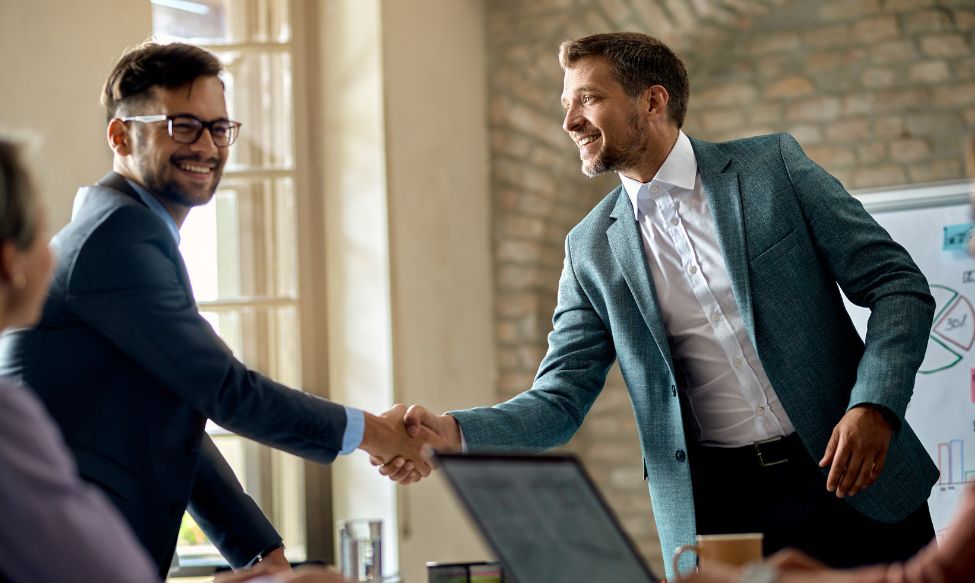 Two business professionals shaking hands in a modern meeting room during a presentation, symbolising partnership, growth and marketing support Ireland, aligned with a results-driven B2B LinkedIn Marketing Strategy 2026.