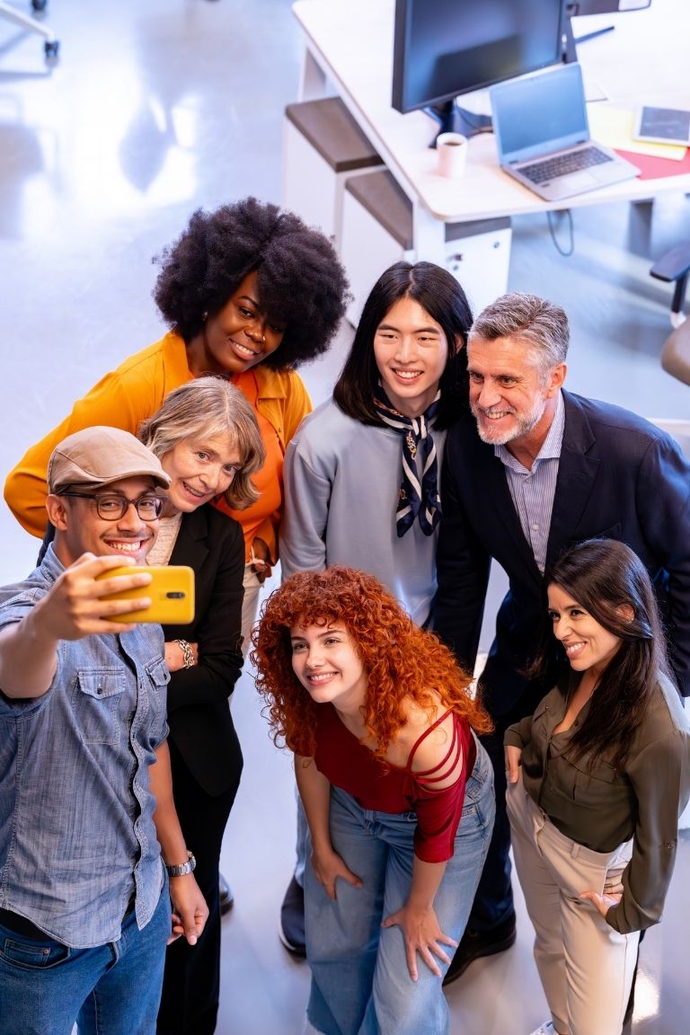 Diverse team of professionals in a modern office taking a group selfie together, smiling and collaborating, representing marketing support Ireland and a forward-thinking B2B LinkedIn Marketing Strategy 2026 approach.