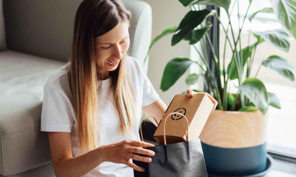 Greenwashing in marketing and packaging, showing a woman unpacking a cardboard product box from a shopping bag, highlighting misleading environmental claims and sustainability messaging.