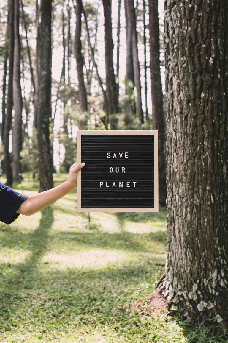 A person holding a ‘Save Our Planet’ sign in a forest, highlighting environmental sustainability, greenwashing and the importance of genuine environmental claims.
